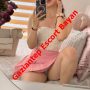 Selfie of a woman in a white lace top and pink skirt posing on a bed, with a red 'Gaziantep Escort Bayan' overlay.